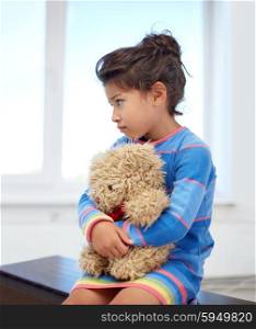 childhood, sadness, loneliness and people concept - sad little girl with teddy bear toy at home