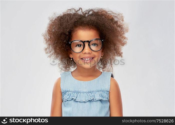 childhood, school and education concept - happy little african american girl in glasses over grey background. happy little african american girl in glasses