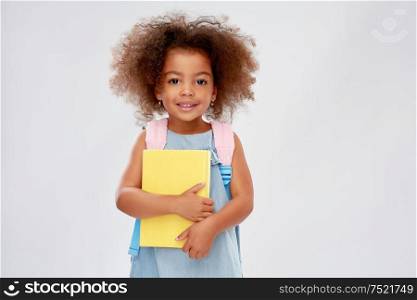 childhood, school and education concept - happy little african american girl with book and backpack over grey background. happy little african girl with book and backpack