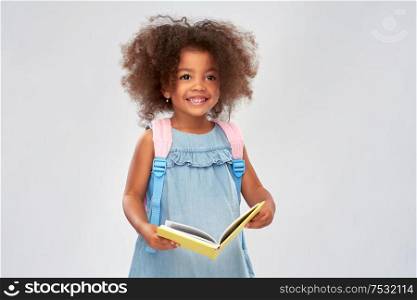 childhood, school and education concept - happy little african american girl with book and backpack over grey background. happy little african girl with book and backpack