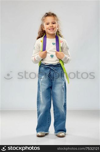 childhood, school and education concept - happy little girl with backpack over grey background. happy little girl with school backpack