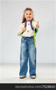 childhood, school and education concept - happy little girl with backpack showing thumbs up over grey background. happy girl with school backpack showing thumbs up
