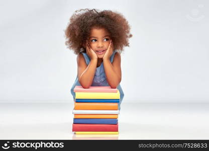 childhood, school and education concept - happy smiling little african american girl with pile of books over grey background. smiling little african american girl with books
