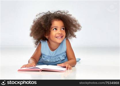 childhood, school and education concept - happy smiling little african american girl reading book over grey background. smiling little african american girl reading book