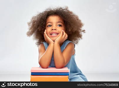 childhood, school and education concept - happy smiling little african american girl with pile of books over grey background. smiling little african american girl with books