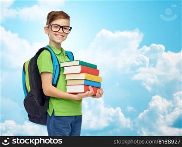 childhood, school, education and people concept - happy smiling student boy in eyeglasses with school bag and books over blue sky and clouds background
