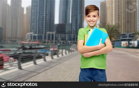 childhood, school, education and people concept - happy smiling student boy with folders and notebooks over dubai city street background