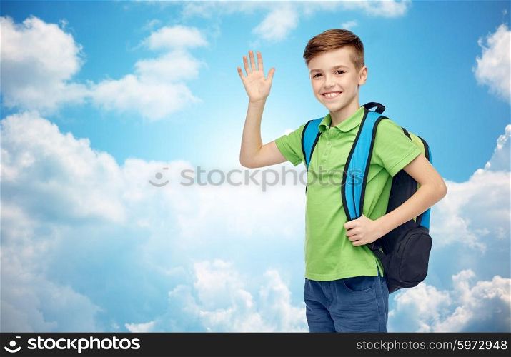 childhood, school, education, greeting gesture and people concept - happy smiling student boy with school bag waving hand over blue sky and clouds background