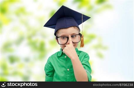childhood, school, education, knowledge and people concept - happy boy in bachelor hat or mortarboard and eyeglasses over green natural background