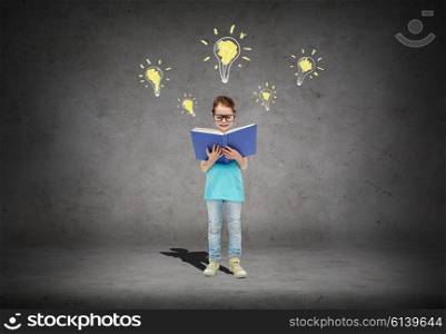 childhood, school, education, knowledge and people concept - happy little girl in eyeglasses reading book over concrete room background with light bulb symbol