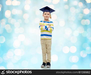 childhood, school, education, learning and people concept - happy boy in bachelor hat or mortarboard over blue holidays lights background