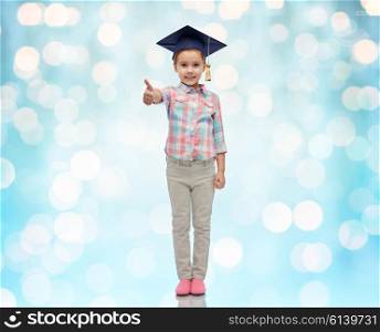 childhood, school, education, learning and people concept - happy girl with in bachelor hat or mortarboard showing thumbs up over blue holidays lights background