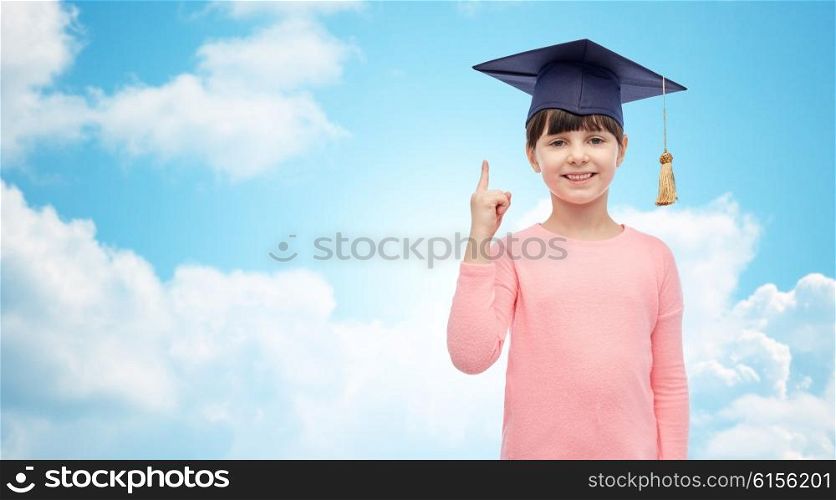 childhood, school, education, learning and people concept - happy girl with in bachelor hat or mortarboard over blue sky and clouds background