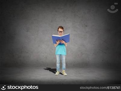 childhood, school, education, vision and people concept - happy little girl in eyeglasses reading book over concrete room background