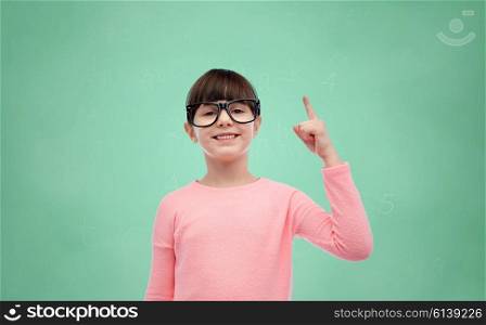 childhood, school, education, vision and people concept - happy little girl in eyeglasses pointing finger up over green school chalk board background