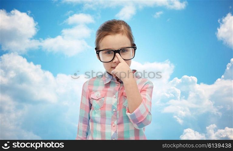 childhood, school, education, vision and people concept - happy little girl in eyeglasses over blue sky and clouds background