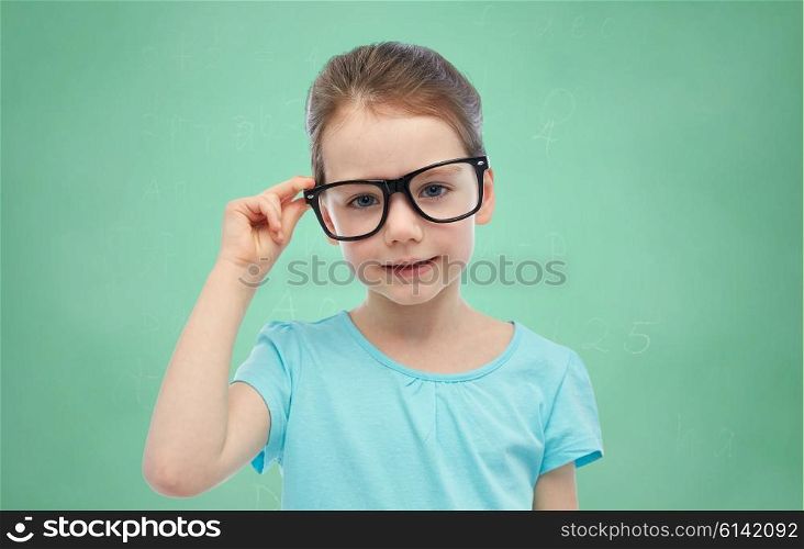 childhood, school, education, vision and people concept - happy little girl in eyeglasses over green school chalk board background