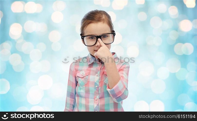 childhood, school, education, vision and people concept - happy little girl in eyeglasses over blue holidays lights background
