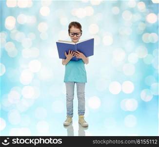 childhood, school, education, vision and people concept - happy little girl in eyeglasses reading book over blue holidays lights background