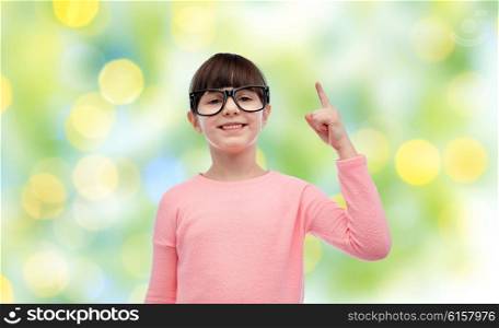 childhood, school, education, vision and people concept - happy little girl in eyeglasses pointing finger up over green lights background