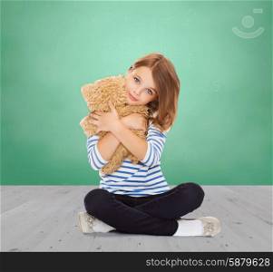childhood, school, toys and people concept - cute little student girl hugging teddy bear over green chalk board background