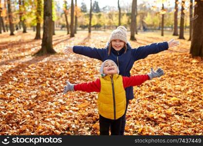 childhood, season and people concept - happy children on fallen leaves at autumn park. happy children at autumn park