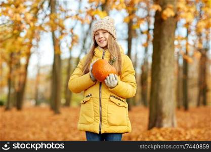 childhood, season and people concept - happy girl with pumpkin at autumn park. happy girl with pumpkin at autumn park