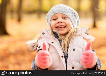childhood, season and people concept - happy little girl at autumn park showing thumbs up. happy little girl at autumn park showing thumbs up