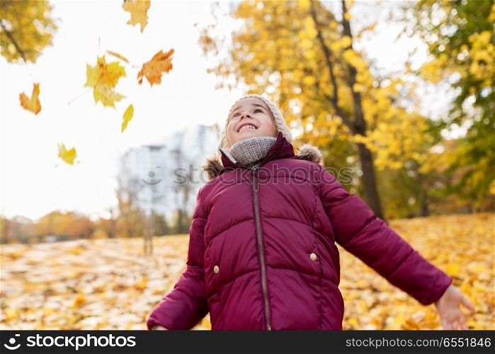 childhood, season and people concept - happy little girl playing with fallen leaves at autumn park. happy girl playing with leaves at autumn park. happy girl playing with leaves at autumn park