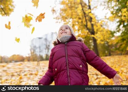 childhood, season and people concept - happy little girl playing with fallen leaves at autumn park. happy girl playing with leaves at autumn park. happy girl playing with leaves at autumn park