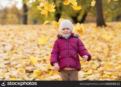 childhood, season and people concept - happy little girl playing with fallen leaves at autumn park. happy girl playing with leaves at autumn park. happy girl playing with leaves at autumn park