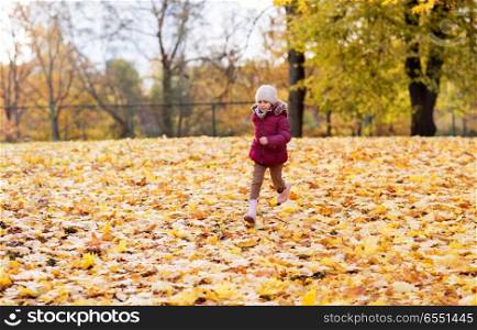childhood, season and people concept - happy little girl running on fallen maple leaves at autumn park. happy girl running at autumn park. happy girl running at autumn park