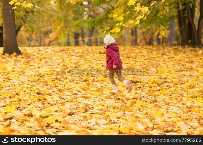 childhood, season and people concept - happy little girl running on fallen maple leaves at autumn park. happy girl running at autumn park