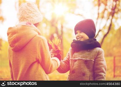 childhood, season and people concept - smiling little girl and boy with autumn leaves in park