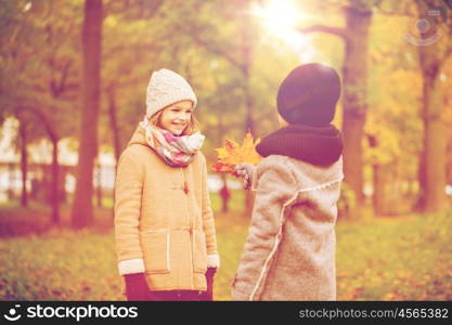 childhood, season and people concept - smiling little girl and boy with autumn leaves in park