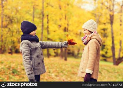 childhood, season and people concept - smiling little girl and boy with autumn leaves in park