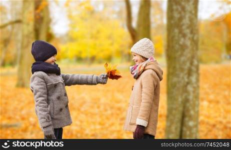 childhood, season and people concept - smiling little girl and boy with autumn leaves in park. smiling children in autumn park