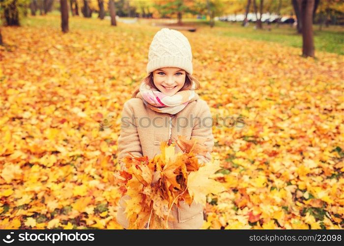 childhood, season and people concept - smiling little girl holding autumn leaves in park
