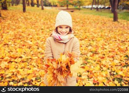 childhood, season and people concept - smiling little girl holding autumn leaves in park