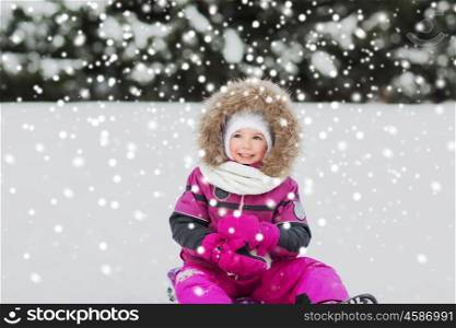 childhood, sledding, fashion, season and people concept - happy little kid on sled outdoors in winter