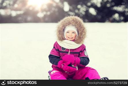 childhood, sledding, fashion, season and people concept - happy little kid on sled outdoors in winter. happy little kid on sled outdoors in winter