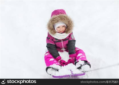 childhood, sledding, fashion, season and people concept - happy little kid on sled outdoors in winter