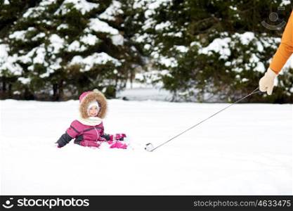 childhood, sledding, fashion, season and people concept - happy little kid riding on sled outdoors in winter