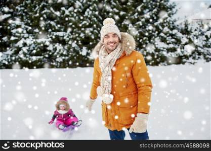 childhood, sledding, leisure, season and people concept - happy man or father carrying little kid on sled in winter