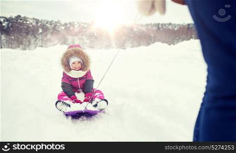 childhood, sledding, leisure, season and people concept - parent carrying happy little kid on sled in winter. parent carrying happy little kid on sled in winter