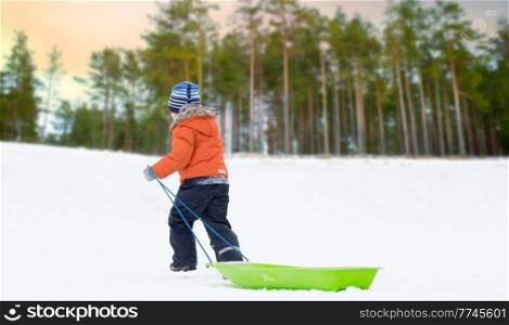 childhood, sledging and season concept - boy with sled climbing snow hill in winter over snowy park or forest background. little boy with sled climbing snow hill in winter