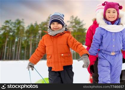 childhood, sledging and season concept - group of happy little children with sleds in winter over snowy forest or park background. happy little children with sleds in winter
