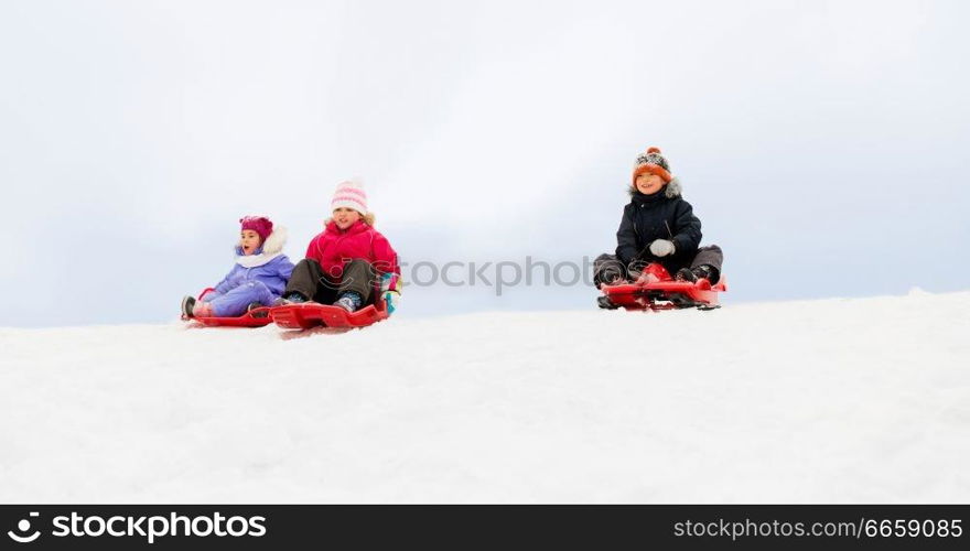 childhood, sledging and season concept - group of happy little kids sliding on sleds down snow hill in winter. kids sliding on sleds down snow hill in winter