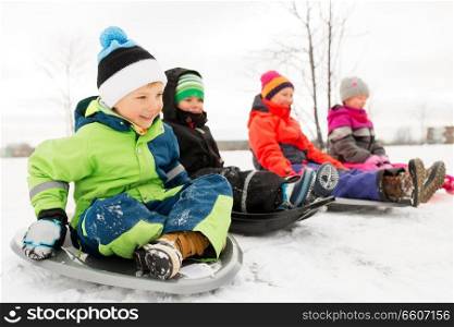 childhood, sledging and season concept - group of happy little kids sliding on sleds in winter. happy little kids sliding on sleds in winter
