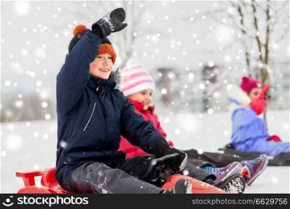 childhood, sledging and season concept - group of happy little kids sliding on sleds in winter. happy kids sliding on sleds in winter